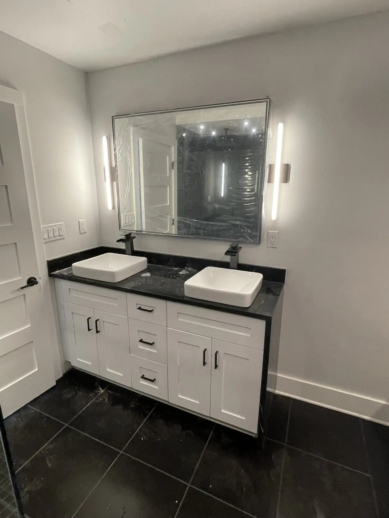 Completed bathroom with a white vanity, dark tile floor, vessel sink, and illuminated mirror