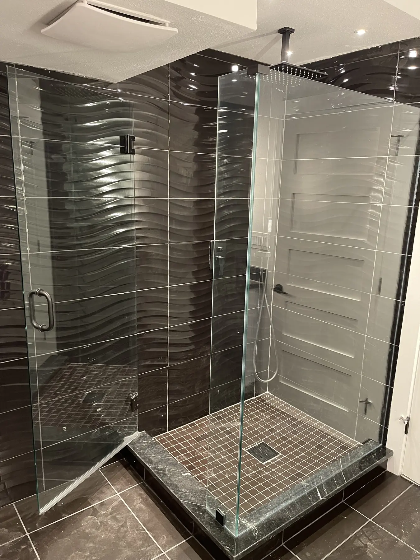 Completed bathroom remodel with a frameless glass shower enclosure and dark textured tile