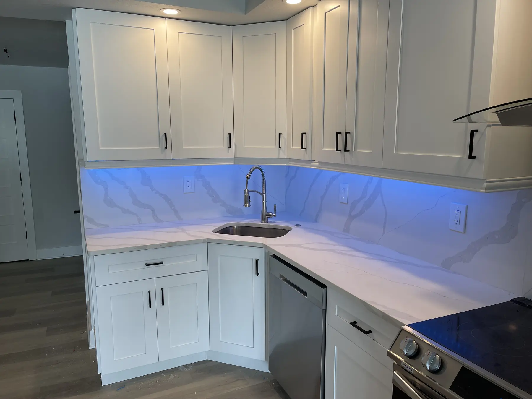Completed white kitchen with under-cabinet lighting and continuous stone-look work surfaces