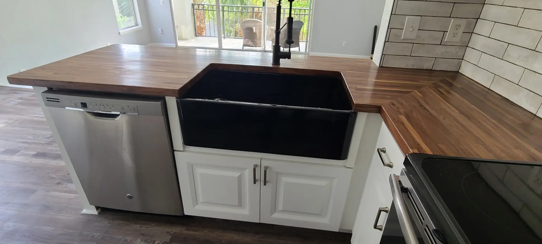 Finished black farmhouse sink installed in a butcher-block counter with white cabinetry