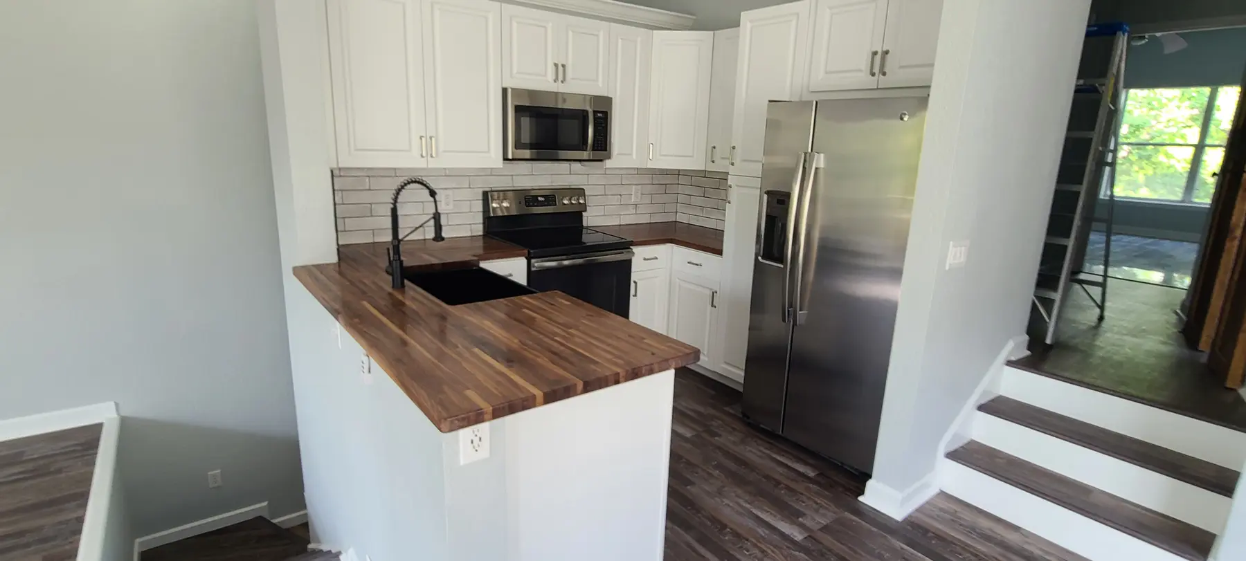 Completed white kitchen with butcher-block countertops and continuous wood-look flooring
