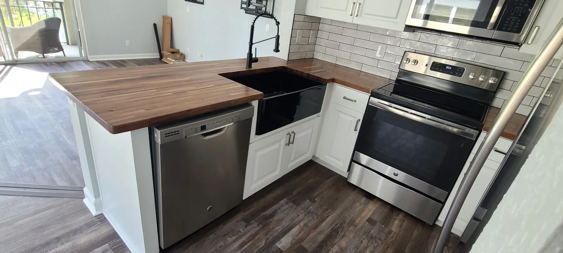 Completed kitchen workspace with white cabinetry, subway tile, dark appliances, and wood-look flooring
